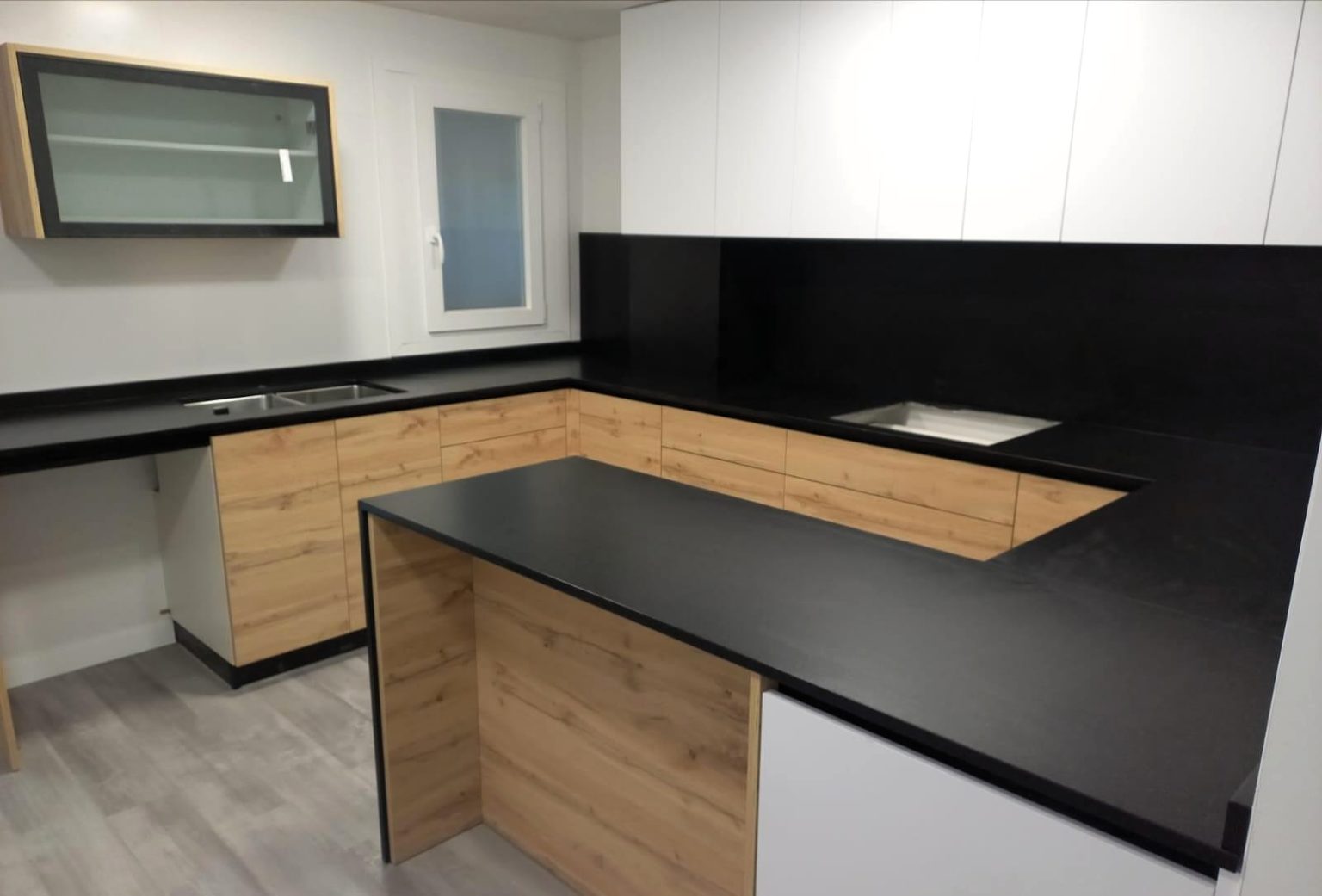 Cocina a medida con isla central, acabado madera y encimera negra en Castellón